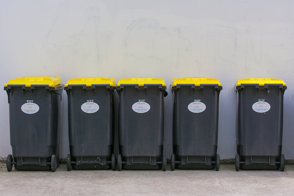 An extensive pile of mixed household waste and discarded packaging materials covers a flat surface. The collection includes crumpled paper, plastic bottles, cans, cardboard boxes, and various plastic